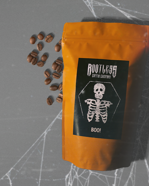 Orange coffee bag with skeleton design labeled 'Boo!' on a spider web background with a shadow of a hand.